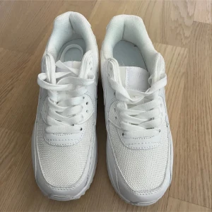 Nike Air max 90 - Säljer ett par helvita Nike sneakers med snörning. Skorna har en klassisk sportig design med rund tå och platt sula. Ovandelen är i mesh och syntet för en luftig känsla. Perfekta för dig som gillar stilrena och bekväma skor.