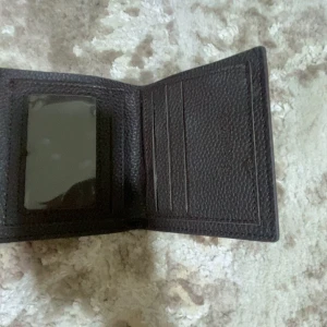 Mörkbrun plånbok f - Säljer en stilren mörkbrun plånbok från . Plånboken har flera kortfack och ett fönster för ID eller foto. Klassisk och tidlös design med präglad yta.