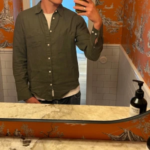 Grön linneskjorta, Arket - Snygg grön linneskjorta från Arket. Skjortan har lång ärm och en avslappnad passform, perfekt att bära över en t-shirt. Enkel och stilren design som funkar till många tillfällen. Använd ett fåtal gånger!!