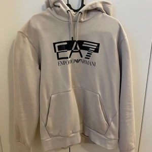 Beige hoodie från Emporio Armani EA7 - Säljer en beige hoodie från Emporio Armani EA7 med svart logga framtill. Storlek är L men passar M