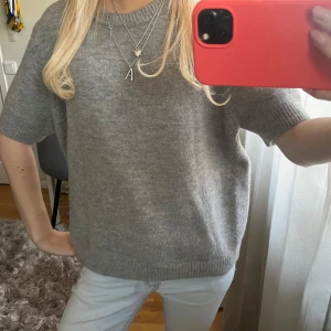 Grå stickad tröja från Zara - Mysig grå stickad tröja från Zara med kortare ärmar och rund halsringning. Perfekt att styla med jeans eller kjol för en enkel och stilren look.