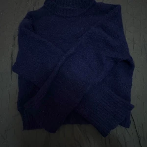 Mörkblå stickad tröja från C - Mysig mörkblå stickad tröja från C med rund hals och långa ärmar. Tröjan har ribbade muddar vid ärmslut och nederkant, perfekt för kyligare dagar. Enkel och stilren design som passar till det mesta.