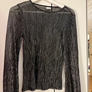 Svart glittrig långärmad topp från Gina Tricot - Säljer en svart långärmad topp från Gina Tricot med glittriga silvertrådar. Tunn och stretchig modell med rund halsringning, perfekt för att sticka ut lite extra. Snygg att styla till både jeans och kjol!