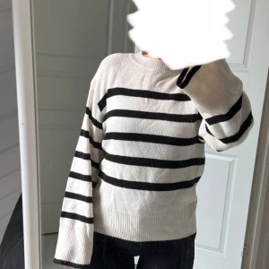 Randig stickad tröja - Säljer en vit/beige stickad tröja med svarta ränder. Tröjan har rund halsringning och långa ärmar med ribbade muddar. Perfekt för en avslappnad och stilren look. Tröjan är ifrån H&M och har använt 1 gång.