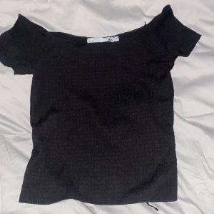 Svart offshoulder topp - Säljer en svart offshoulder topp med korta ärmar. Enkel och stilren design som passar perfekt till många olika outfits. Toppen har en tight passform och är gjord i ett stretchigt material.