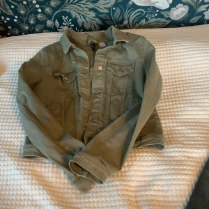 Olivgrön jacka från Hm - Säljer en snygg olivgrön jacka från hm i storlek 40. Jackan har en klassisk jeansjacka-look med knappar framtill och långa ärmar. Perfekt för höst och vår, och funkar både till vardags och fest. Den är i bra skick och använd fåtal gånger, säljer då den är för liten😊🥂🥰