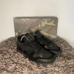 Valentino Rockrunners - Säljer ett par Valentino Rockrunner sneakers i svart och grått camouflagemönster. Skorna har svarta snören, rund tå och platt sula. Märkeslogga på plösen och detaljer i skinn och mocka. Kommer med originalkartong.