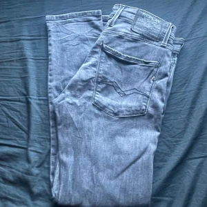 Replay anbass  - Säljer ett par grå jeansbyxor från Replay med klassisk femficksdesign och raka ben. Byxorna har normal passform och är tillverkade i mjukt denimtyg. Perfekta för en avslappnad stil. Skicket är 7/10, storlek W31 L32 slimfit 