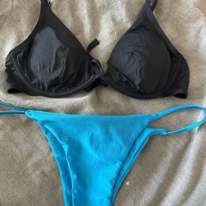 Svart och blå bikini med knyt - Tvådelad bikini med svart trekantsöverdel som har knyt i ryggen och smala axelband. Underdelen är blå med tunna sidoband. Enkel och stilren design, perfekt för stranden eller poolen. Topp från Lindex och underdel från shein. ENDAST TESTAD!