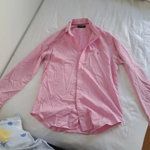 Rosa skjorta från Polo Ralph Lauren - Snygg rosa skjorta från Polo Ralph Lauren i slim fit-modell. Skjortan har klassisk krage, långa ärmar och knäppning framtill. Broderad logga med polospelare på bröstet. Perfekt för dig som gillar stilrena och tidlösa plagg. Köpt för 1750