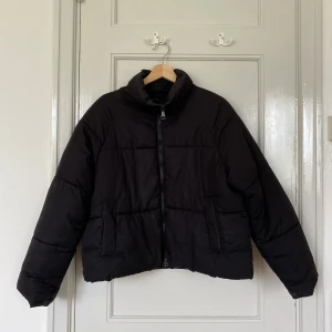 svart pufferjacka från monki - svart pufferjacka från monki i storlek S. jackan har hög krage, raka ärmar, dragkedja framtill och två fickor på sidorna. perfekt för kalla dagar när du vill ha en stilren och enkel look!
