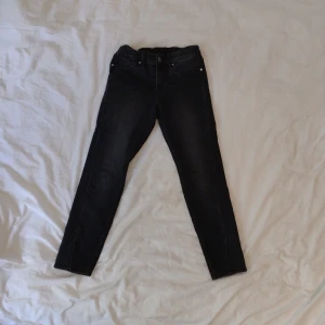 Svarta skinny jeans i denim, stl 140 - Svarta skinny fit jeans från &Denim i storlek 140. Klassisk femficksmodell med stretchig passform och resår i midjan. Jeansen har en mörk tvätt och är tillverkade i mjukt denimtyg. Perfekta för dig som gillar en smal siluett. Slitt nertill på benen (se bild).