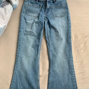Ljusblå bootcut jeans med fickor - Säljer ett par ljusblå jeans med bootcut-modell och klassiska bakfickor. Jeansen har bälteshällor och dragkedja framtill. Perfekta för dig som gillar en retro vibe och vill ha ett par snygga jeans med lite utsvängda ben. Aldrig använda org pris 500. storlek xs fast passar mig som har s eftersom de är ganska stretchiga 