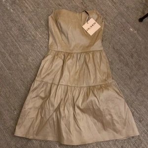 Champagnefärgad axelbandslös klänning - Superfin axelbandslös klänning i champagnefärg från Girl In Mind. Klänningen har en volangig kjol med flera lager och en snygg. Jag har klippt av armarna ( se bild två ) inget som syns på🫶🏼