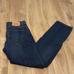 Grant Regular Fit jeans blå 34/34 - Snygga blå jeans från Grant i regular fit med klassisk femficksdesign och kontrastsömmar. Jeansen har rak passform och är tillverkade i slitstarkt denim med tydlig struktur. Perfekta för dig som gillar en tidlös och enkel look.