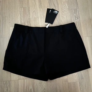 Svarta shorts från Weekday - Stilrena svarta shorts från Weekday med klassisk passform och bälteshällor. De har en rak siluett och diskreta fickor både fram och bak. Perfekta för en clean och enkel look. Materialet känns mjukt och svalt, perfekt för varmare dagar.