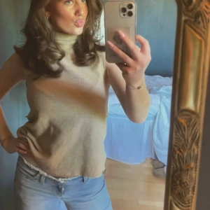 Beige ärmlös polotopp - Säljer en stilren beige polotopp utan ärmar. Toppen har en hög hals och är i ett mjukt, stickat material. Den är knappast använd!