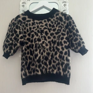 Leopardmönstrad stickad tröja S - Supermjuk stickad tröja med leopardmönster i svart och beige. Tröjan har rund halsringning, puffiga halvlånga ärmar och ribbade muddar. Perfekt för dig som vill sticka ut med en trendig och djurinspirerad look. Från NAKD i storlek S 