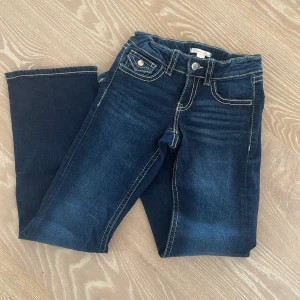 Mörkblå jeans från Gina Tricot stl 152 - Snygga mörkblå jeans från Gina Tricot med kontrastsömmar och coola fickdetaljer bak. Klassisk femficksmodell med knäppning fram och raka ben. Perfekta för dig som gillar en stilren look med lite edge.