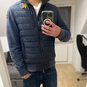 Parajumper cardigan - Säljer en snygg blå jacka/cardigan från Parajumpers. Perfekt för kyligare dagar med sin fleece och puffer kombination. Det finns en liten fläck på vänster ärmen. Ny pris 4600kr