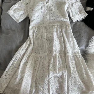 Vit broderad kortklänning i bomull från mango - Superfin vit kortklänning i broderad bomull med v-ringning och korta ärmar. Klänningen har volang i kjolen och ett vackert hålbroderat mönster som ger en romantisk vibe. Perfekt för varma dagar och somriga tillfällen. Nypris 799kr