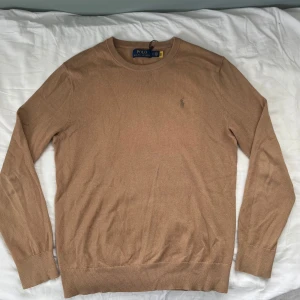 Ralph lauren stickad tröja  - Snygg beige stickad tröja från Polo Ralph Lauren 8% Kashmir och 92% bomull så mjuk o skön, med klassisk rund hals och diskret broderad logga på bröstet. Långärmad modell i mjukt material som passar perfekt till jeans eller chinos. Enkel och stilren design som funkar året runt.