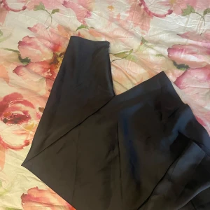 Svart lång satinkjol med dragkedja - Säljer en svart långkjol i satin med snyggt fall och diskret glans. Kjolen har en smal passform och stängs med dragkedja i sidan. Perfekt för dig som gillar en clean och stilren look.