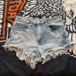 Midwhaist  jeansshorts från H&M Divided - Snygga ljusblå jeansshorts från H&M Divided i storlek 38. De är midwhaist  med fransig och sliten kant, klassiska fem fickor och dragkedja med knapp. Perfekta för sommaren och ger en cool, avslappnad vibe.
