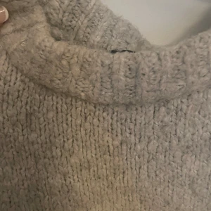Beige stickad polotröja - Mysig grå stickad polotröja med grovstickad struktur och hög krage. Perfekt för kyliga dagar och enkel att matcha med jeans eller kjol. Tröjan har lång ärm och en avslappnad passform som ger en chill vibe.