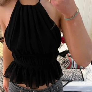 Svart omlott halterneck topp med volang - Säljer en superfin svart halterneck topp med omlott och knyt i ryggen. Toppen har typ volangkant nertill , luftig och tunt, material. Orginalpriset va 300 kr ca. Aldrig använd men gammal topp som bara hängt i garderoben, jätte söt.
