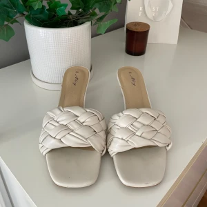 Vita flätade sandaler från Alley - Snygga sandaler från Alley i vitt med breda, flätade remmar och fyrkantig tå. Skorna har låg klack, använda 3 gånger, fått någon typ av vattenskada som syns på bild 4