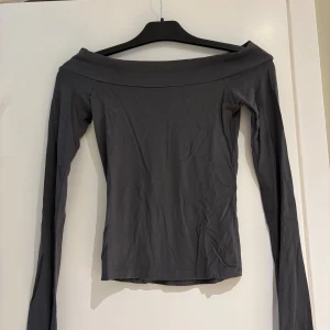 Grå offshoulder topp från BikBok - Snygg grå offshoulder topp från BikBok i stretchigt material. Långärmad och figurnära modell som sitter snyggt över axlarna. Perfekt att styla med jeans eller kjol för en trendig look.