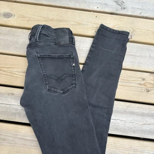Replay Anbass svarta jeans - Snygga svarta Replay Anbass jeans med klassisk femficksdesign och diskreta sömmar på bakfickorna. Jeansen har en smal passform och är tillverkade i stretchig bomullsdenim för extra komfort. Perfekta för dig som gillar en stilren och modern look.