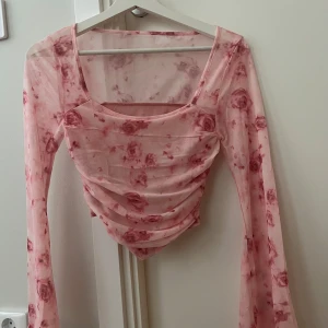 Rosa mesh blommig topp med rynk - Säljer en superfin rosa mesh topp med blommigt mönster i rött. Toppen har långa ärmar, fyrkantig ringning och snygga rynkdetaljer framtill. Den är croppad och har en lätt transparent känsla som ger en trendig vibe.