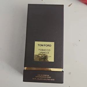 Tom Ford Tobacco Vanille 100 ml EdP - Tom Ford Tobacco Vanille Eau de Parfum 100 ml. Lyxig parfym i svart, fyrkantig flaska med guldfärgad etikett och detaljer. Doften kombinerar tobak och vanilj för en varm, kryddig och söt känsla. Kommer i elegant mörkbrun kartong med gulddetaljer.