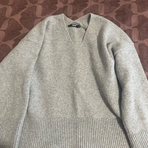 Grå stickad v-ringad tröja BikBok - Mysig grå stickad tröja från BikBok i storlek S. Tröjan har v-ringning, långa ärmar och bred ribbad kant nedtill. Perfekt för lager-på-lager och chill dagar. Enkel att matcha med jeans eller kjol.