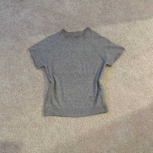 Kortärmad stickad tröja - Supermjuk grå stickad tröja från Vero Moda i storlek XS. Tröjan har korta ärmar, rund halsringning och ribbade detaljer vid hals och nederkant. Tröjan var från början långärmad, men har själv klippt ärmarna korta. Tycker inte att den sitter bra på mig och kommer därför inte att skicka bilder när jag har den på mig💓💓