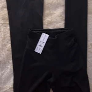 Svarta höga leggings med bootcut - Svarta leggings med hög midja och bootcut-ben. Snygg och enkel design som passar perfekt till sneakers eller chunky boots. Stretchigt material som sitter skönt och följer kroppen. Perfekta för dig som gillar en clean och stilren look.