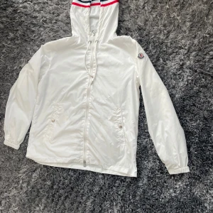 Moncler windbreaker - Snygg vit vindjacka från Moncler med huva och dragsko. Jackan har dragkedja framtill, två fickor med knappar och elastiska muddar. Pris kan diskuteras!