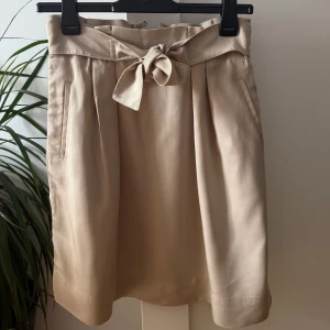 Beige kjol från HM - Säljer en snygg beige kjol från H&M med  knytband framtill. Kjolen har fickor i sidorna och dragkedja bak. 