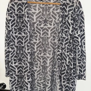 Svartvit kofta med stjärnmönster H&M - Säljer en svartvit kofta från H&M Divided i storlek S. Koftan har ett unikt grafiskt stjärnmönster och är tillverkad i en mjuk blandning av viskos och polyester med lite stretch. Den har lång ärm och öppen front, perfekt att slänga på över en t-shirt eller topp.