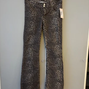 Leopardmönstrade bootcut jeans Nelly - Snygga bootcut jeans från Nelly med leopardmönster i bruna och svarta toner. Byxorna har låg midja, klassisk femficksdesign och dubbla silverknappar framtill. Perfekta för dig som vill sticka ut med ett djurmönstrat statement. Storlek 40 men passar mer som 36/38. Köpte för 600kr