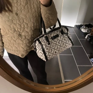 Vit och svart handväska - Snygg handväska från Giulia Pieralli i vit och svart med rutigt mönster. Väskan har svarta detaljer i skinnimitation, dubbla handtag, avtagbar axelrem och dragkedja upptill. Den är väldigt rymlig och får plats med det mesta. Mått: 28x18 