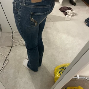 Blå bootcut jeans från Hollister - Snygga blå jeans från Hollister med bootcut passform och klassiska kontrastsömmar. Låg midja och coola detaljer på bakfickorna. Jeansen är i stretchigt denim som sitter tajt upptill och släpper ut vid benslutet. Midjemått:37cm och innerbenslängd: cirka 72cm❤️