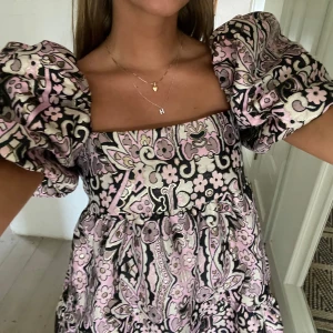 & other stories klänning - Superfin kortklänning med blommigt mönster i lila, svart och beige. Klänningen har fyrkantig urringning och stora puffärmar som ger en trendig look. Använd 1 gång