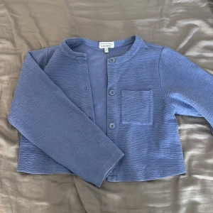 Blå cardigan jacka från A.P.C. - Snygg blå cardigan jacka från A.P.C. med rund halsringning, knappar framtill och en bröstficka. Jackan har en croppad passform och är tillverkad i ett strukturerat tyg som ger en cool känsla. Perfekt för lager-på-lager och enkel att styla.