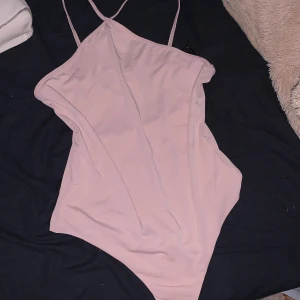 Ljusrosa bodysuit från H&M - Supersnygg ljusrosa bodysuit från H&M med tunna axelband och enkel, stilren design. Perfekt att styla med jeans eller kjol för en clean look. Mjuk och stretchig i materialet för en bekväm passform. Den är aldrig använd då den var för liten när jag testade den. 