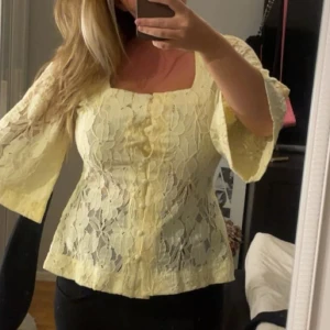 Gul spetsblus från NA-KD - Superfin ljusgul blus från NA-KD i spets med stora blommönster. Blusen har vida trekvartsärmar, fyrkantig ringning och klädda knappar framtill. Perfekt för dig som vill ha en romantisk och trendig look.