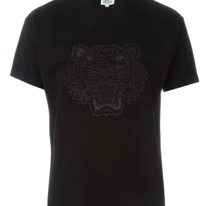 Svart Kenzo t-shirt med tigerbrodyr - Svart t-shirt från Kenzo med ikonisk tigerbrodyr framtill. Klassisk passform med korta ärmar och rund halsringning. Perfekt för dig som vill ha en stilren men ändå edgy look. Storlek xs men den är lite större i storleken så den är som en S. Passar både killar och tjejer. tveka inte på att skriva till mig om ni har några funderingar eller vill ha mer bilder på tröjan.