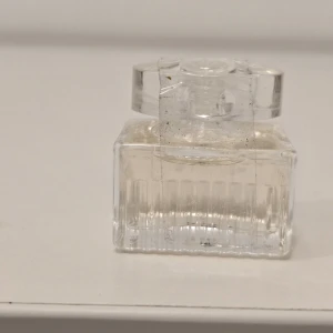 Chloé parfym miniflaska - Söt miniflaska från Chloé med elegant, transparent design. Flaskan är rektangulär med räfflade sidor och har ett genomskinligt lock där Chloé-loggan syns. Perfekt att ha med i väskan för en fräsch doft när som helst.